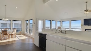 A modern kitchen with a large island, built-in dishwasher, and a view of the ocean. - Beachfront Dolphin by Ryson Vacation Rentals (Galveston)