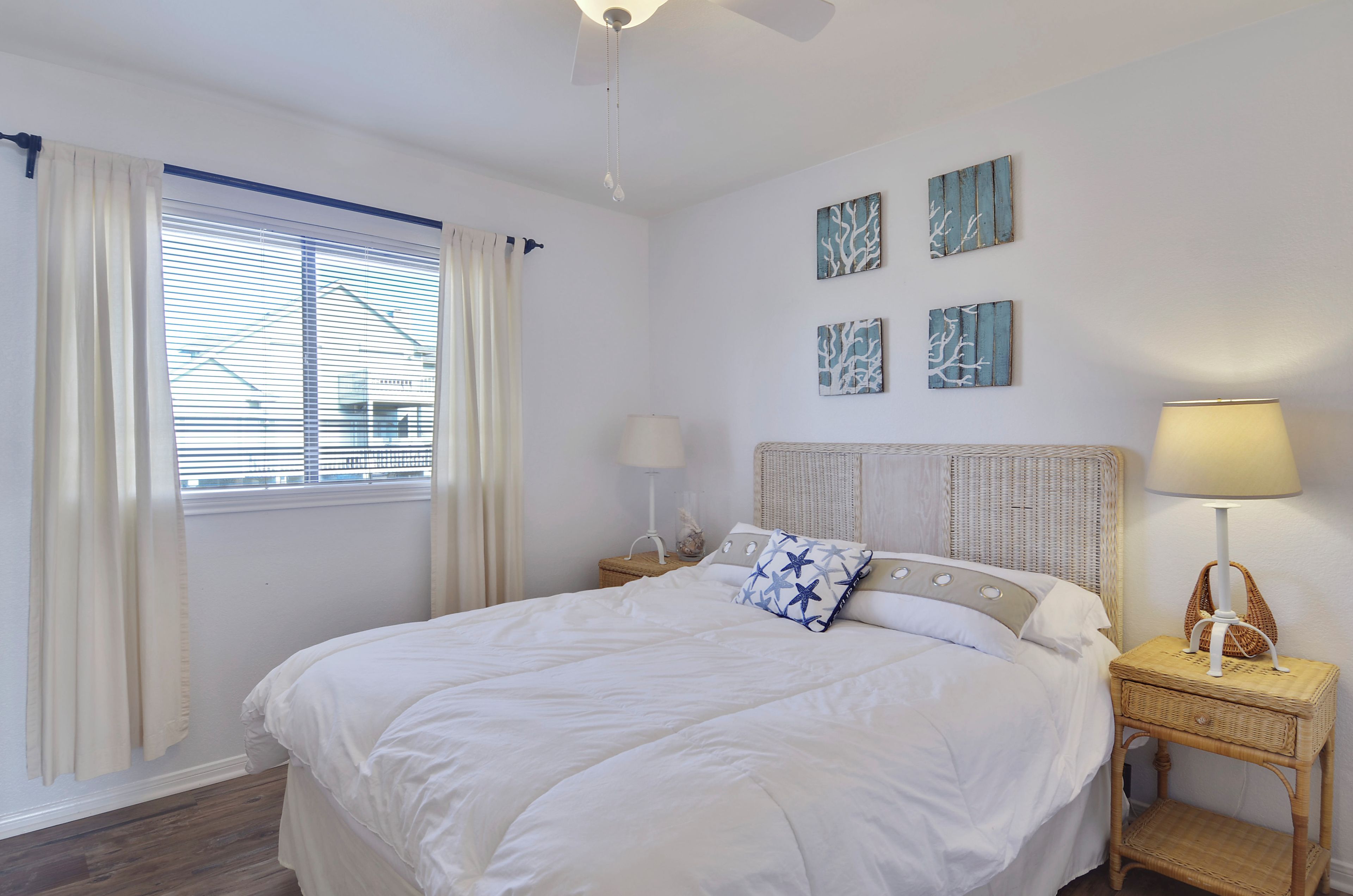 A neatly made bed with white bedding, a bedside table with a lamp, and a window with curtains.
