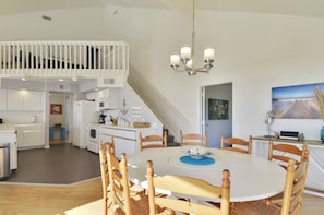 A modern kitchen with white cabinetry, a dining area with a round table and wooden chairs, and a staircase leading to an upper level. - Beachfront Dolphin by Ryson Vacation Rentals (Galveston)