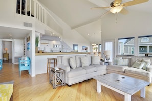 A spacious living area with a high ceiling, a large sofa, a coffee table, and a kitchen area in the background. - Beachfront Dolphin by Ryson Vacation Rentals (Galveston)