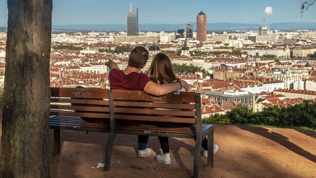Una pareja sentada en un banco admirando una vista urbana con edificios y cielo despejado.