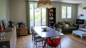 Una sala moderna con una mesa de comedor, sillas, un sillón rojo, una estantería, un sofá y una ventana con cortinas.