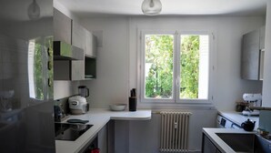 Una cocina moderna con armarios blancos, horno empotrado, hervidor y ventana con vista a la vegetación.