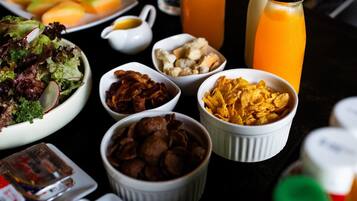 Uma mesa com diversos alimentos, incluindo salada, bacon, cereais e uma garrafa de suco de laranja.