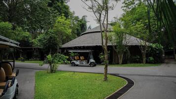 A golf cart parked near a thatched-roof building surrounded by lush greenery.
