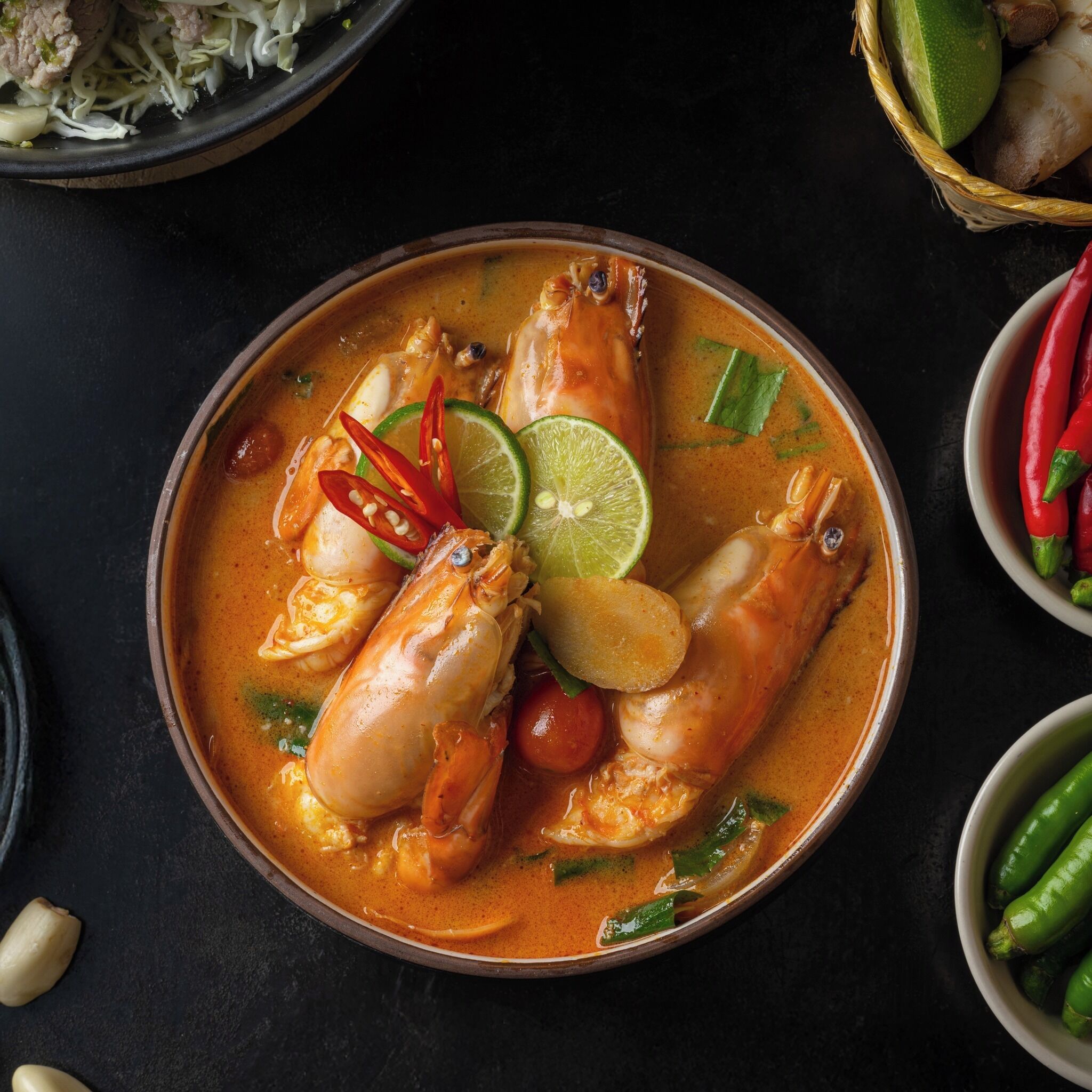 Uma tigela de sopa de marisco com camarão, decorada com limão e pimenta.