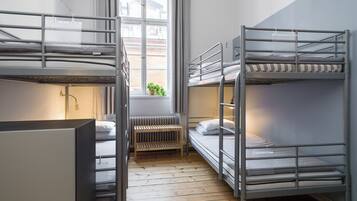 Un dormitorio con literas, un radiador, un ventanal con cortinas y una planta pequeña en el alféizar.