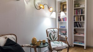 Eine gemütliche Leseecke mit einem Sessel, einem kleinen Tisch mit Teekanne und Tassen sowie einem Bücherregal voller Bücher.