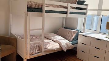 A bunk bed with striped bedding, a wooden desk with drawers, a chair, and a window with blinds.