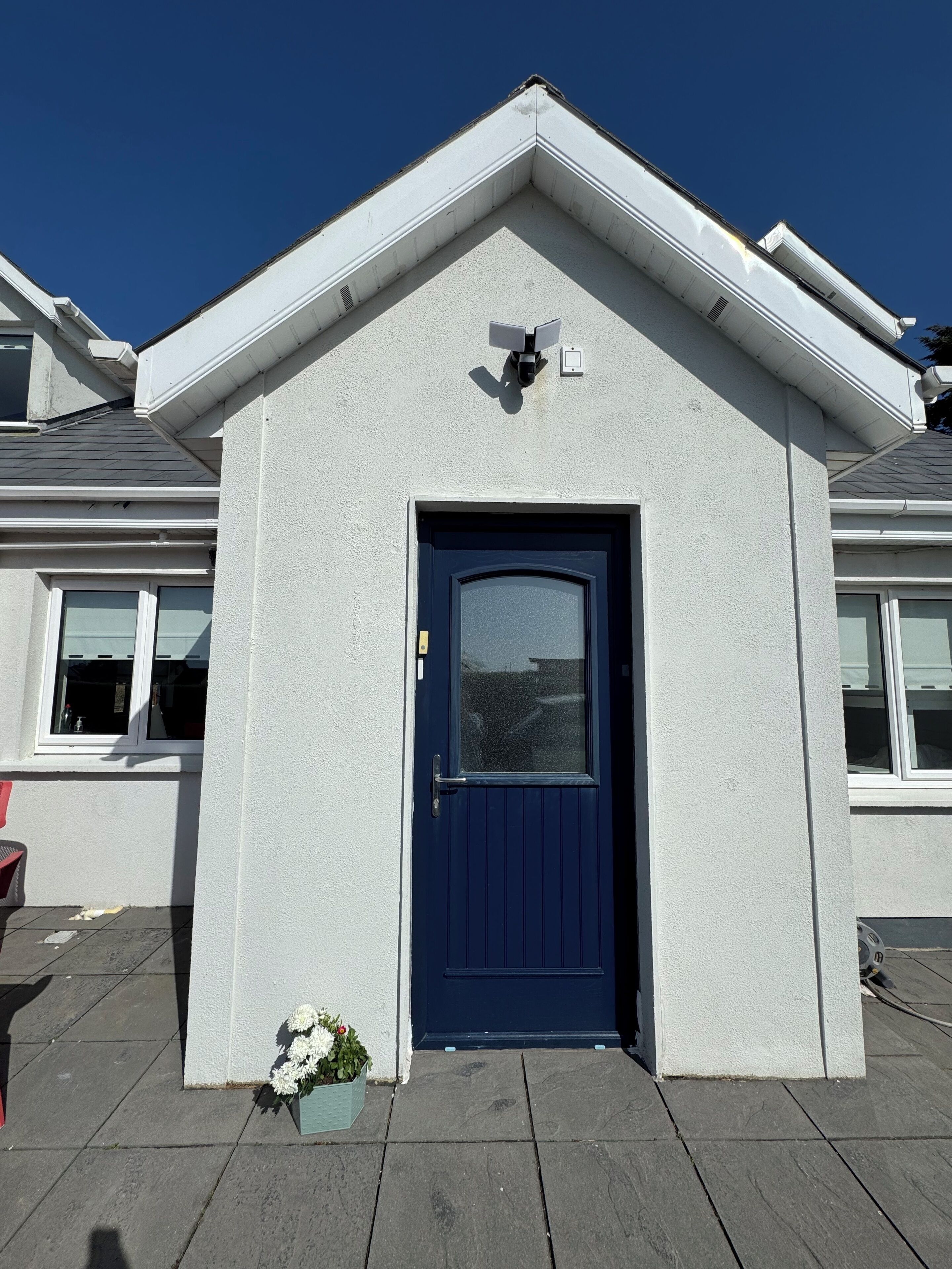 A house with a dark blue door, a small porch with a flower pot, and a security camera above the door.