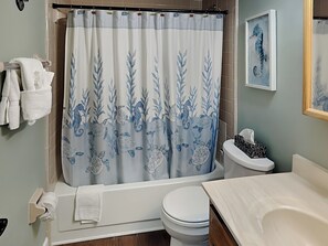 A bathroom with a shower curtain featuring sea turtle and seahorse designs, a toilet, a sink, and a towel rack with towels. - Starboard Light 7 by Distinctive Beach Rentals (Ormond Beach)