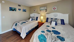 Ein Schlafzimmer mit zwei Betten, beige gefärbten Wänden und Kunstwerken.