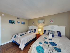 A bedroom with two beds, beige walls, and artwork. - Starboard Light 7 by Distinctive Beach Rentals (Ormond Beach)