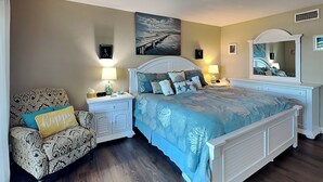 A bedroom with a bed, nightstands, a chair, and a large mirror. - Starboard Light 7 by Distinctive Beach Rentals (Ormond Beach)