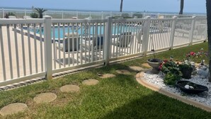 A pool area with a white fence, lounge chairs, and a view of the ocean. - Starboard Light 7 by Distinctive Beach Rentals (Ormond Beach)