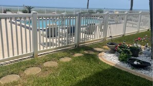 Ein Poolbereich mit weißem Zaun, Liegestühlen und Blick aufs Meer.