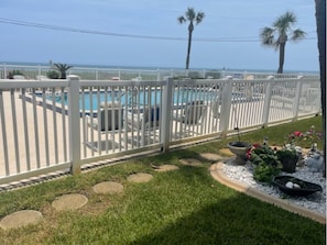A pool area with a white fence, lounge chairs, and a view of the ocean. - Starboard Light 7 by Distinctive Beach Rentals (Ormond Beach)