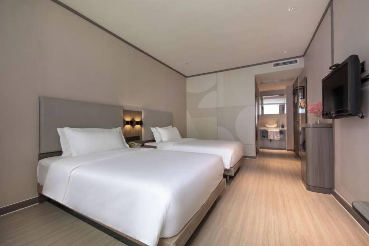 A hotel room with two beds, a TV, and a bathroom visible through an open door.