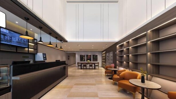 Een moderne hotellobby met een receptiebalie, zithoek en een groot digitaal scherm.