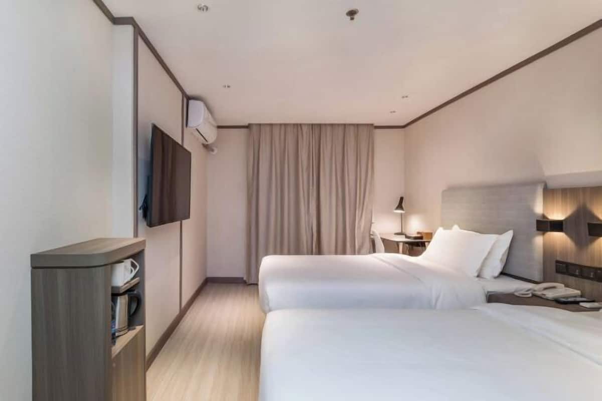 Quarto de hotel com duas camas, televisão, mesa de cabeceira com abajur e minibar.