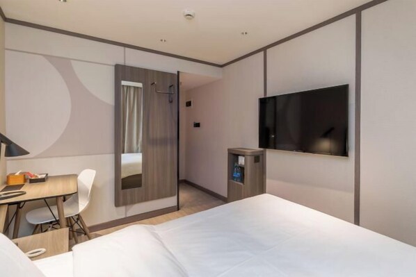 Ein modernes Hotelzimmer mit Bett, Schreibtisch, Stuhl, Fernseher und Kleiderschrank.