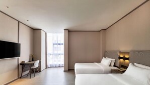 Een hotelkamer met twee bedden, een televisie, een bureau met stoel en een groot raam.