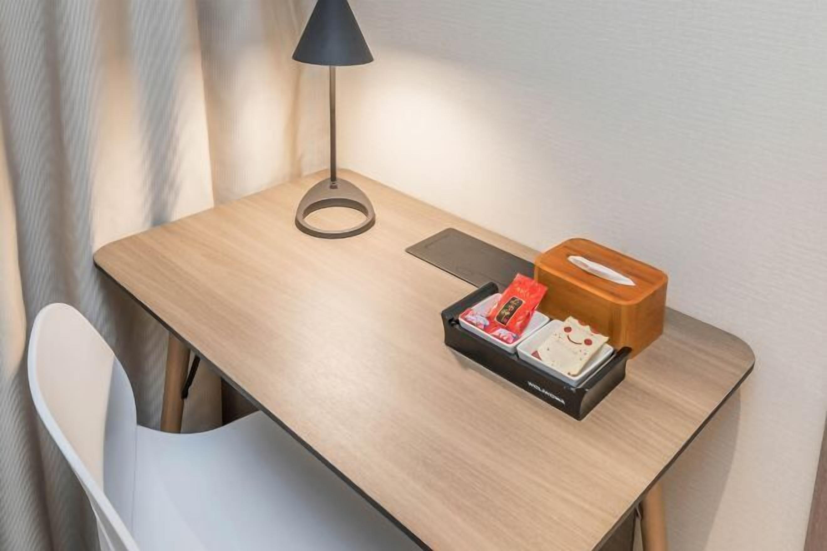 A wooden desk with a lamp, a tray with snacks, and a tissue box.