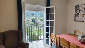 Een kamer met balkon, een eettafel met stoelen en een bank.
