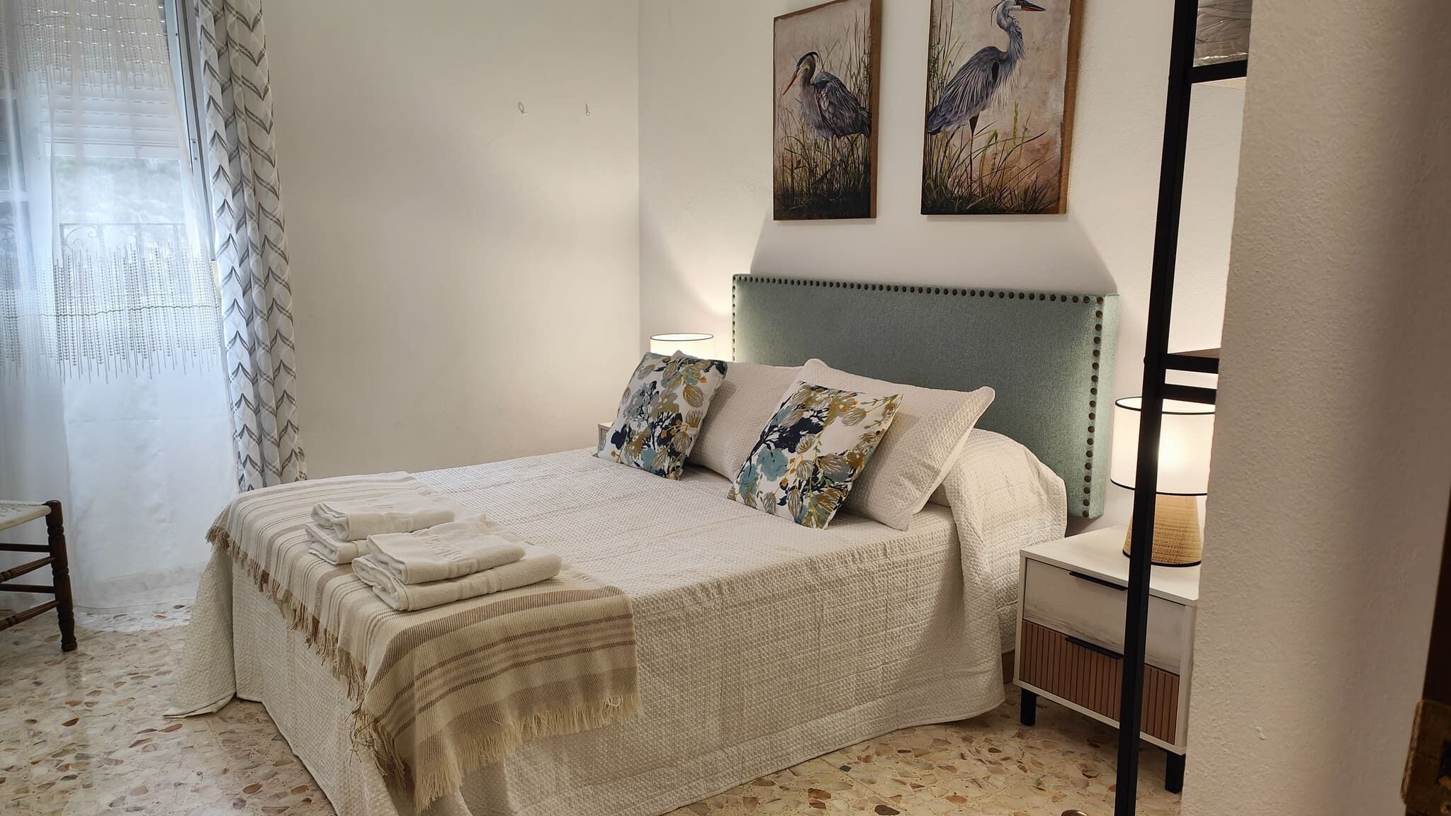 A neatly made bed with a striped blanket, two pillows with a floral pattern, and a headboard.