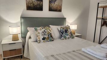 Un dormitorio ordenado con una cama, dos mesitas de noche y dos lámparas.