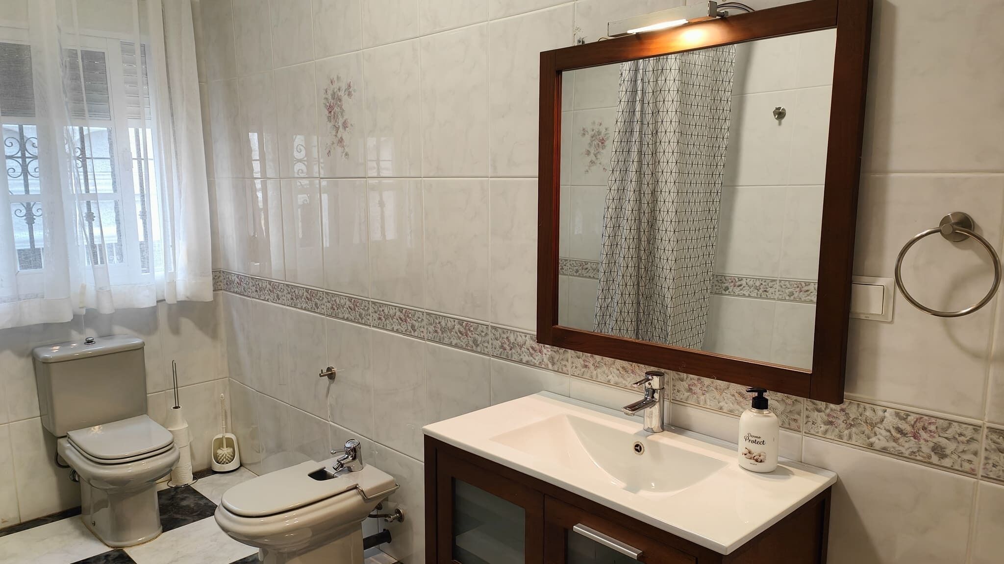 Un baño con inodoro, bidé, lavamanos y espejo.