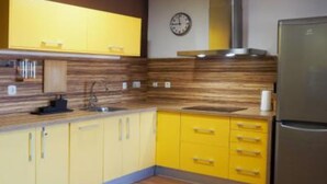 Een keuken met gele kastjes, een roestvrijstalen koelkast en een houten achterwand.