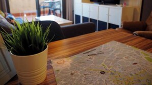 Een woonkamer met een houten tafel, een potplant, een kaart en een televisie op een wit kastje.