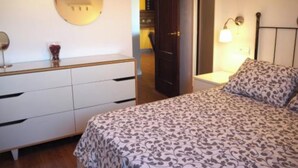 Een slaapkamer met een bed, een dressoir, een spiegel en een wandlamp.