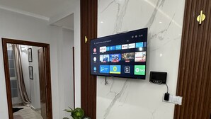 Eine moderne Hotelhalle mit Marmorwand, einem montierten Fernseher, der verschiedene Streaming-Dienste zeigt, und einem Blumentopf.