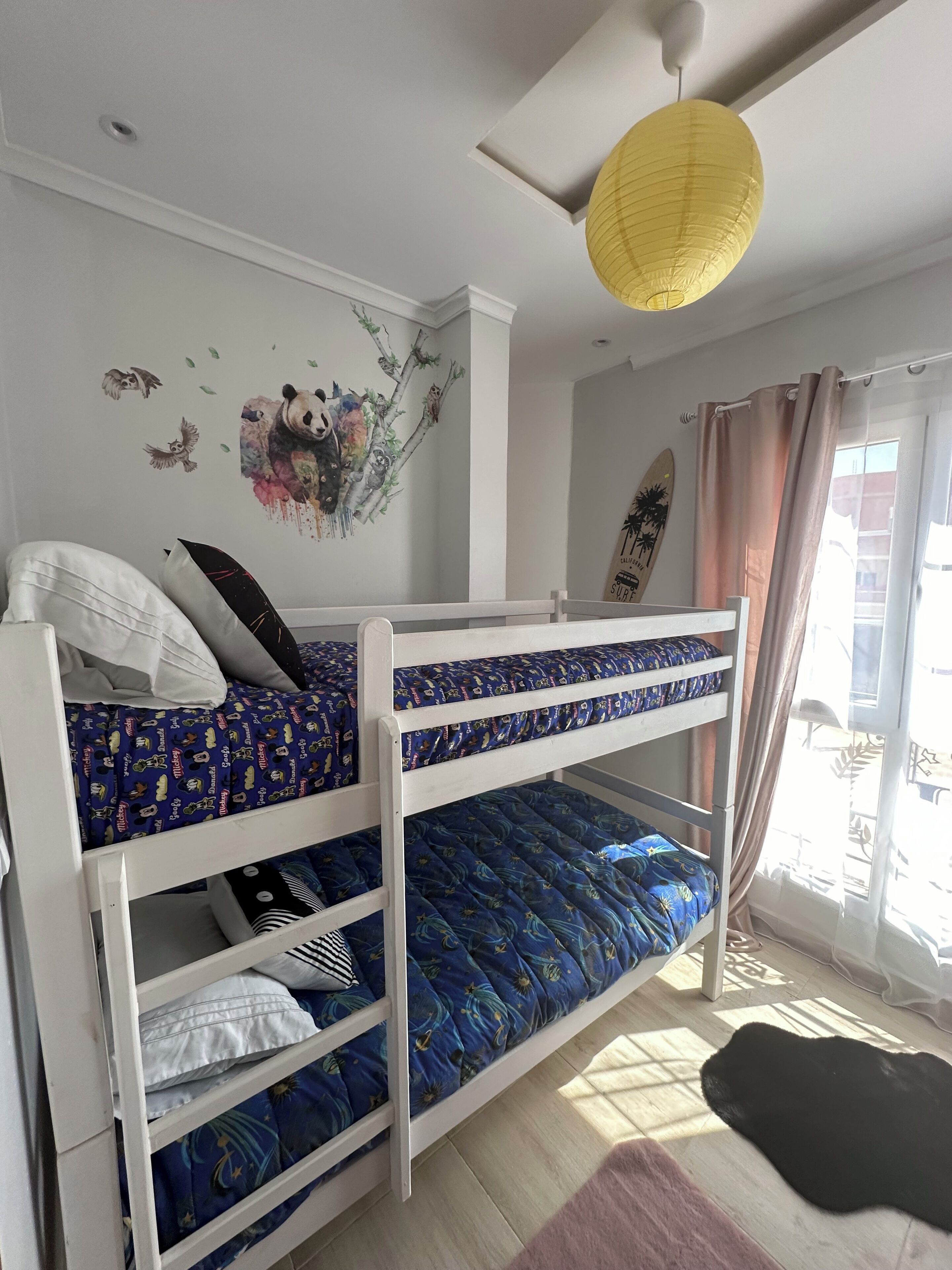 A bunk bed room with a panda wall decal, a surfboard decoration, and a yellow hanging light.