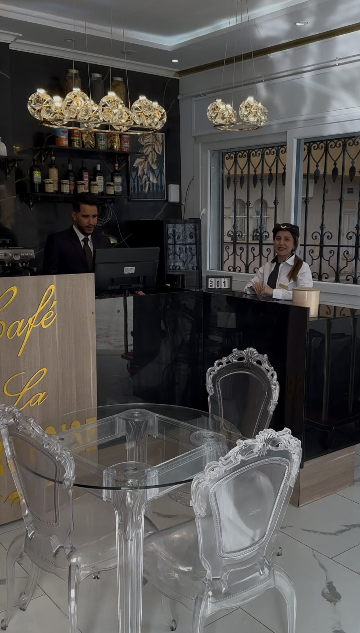 Un espace bar doté d’un comptoir en bois, d’une table en verre avec des chaises et d’un lustre décoratif.
