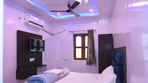 Un dormitorio con cama, ventilador de techo, unidad de aire acondicionado, televisor y ventana con cortinas.