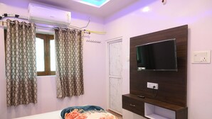 Un dormitorio con cama, televisión montada en la pared, ventana con cortinas y equipo de aire acondicionado.