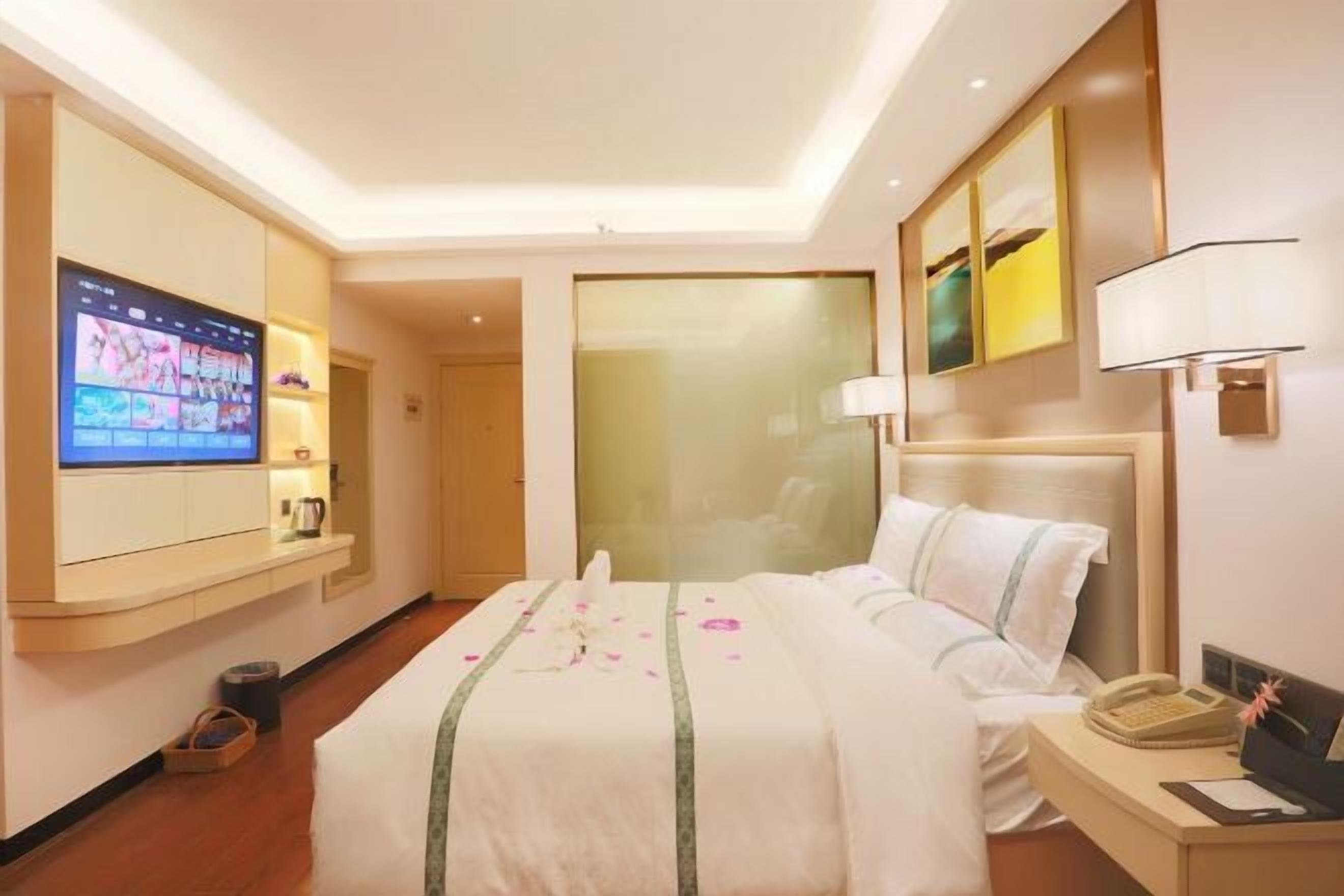 A hotel room with a bed, a TV, a desk with a lamp, and artwork on the wall.