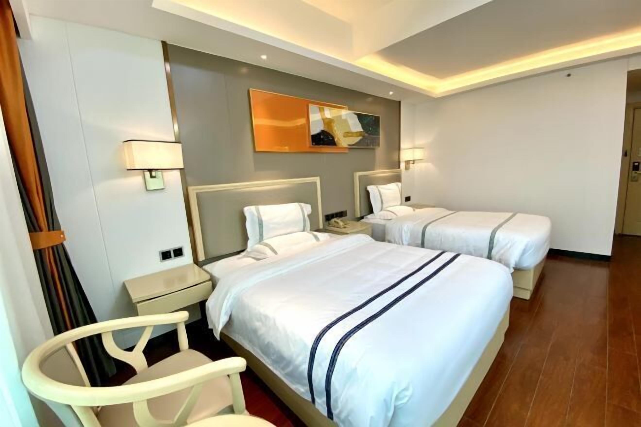 A hotel room with two beds, a desk, a chair, and a mirror.