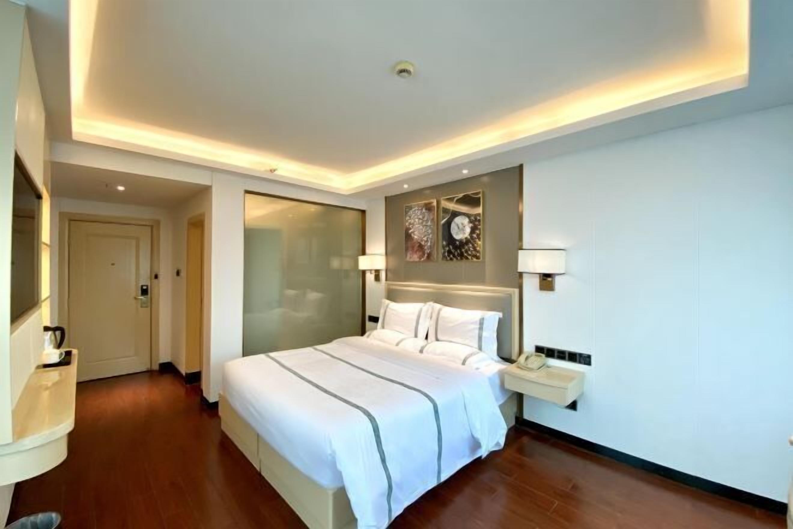 A modern hotel room with a large bed, bedside lamps, a nightstand, and a wall-mounted phone.