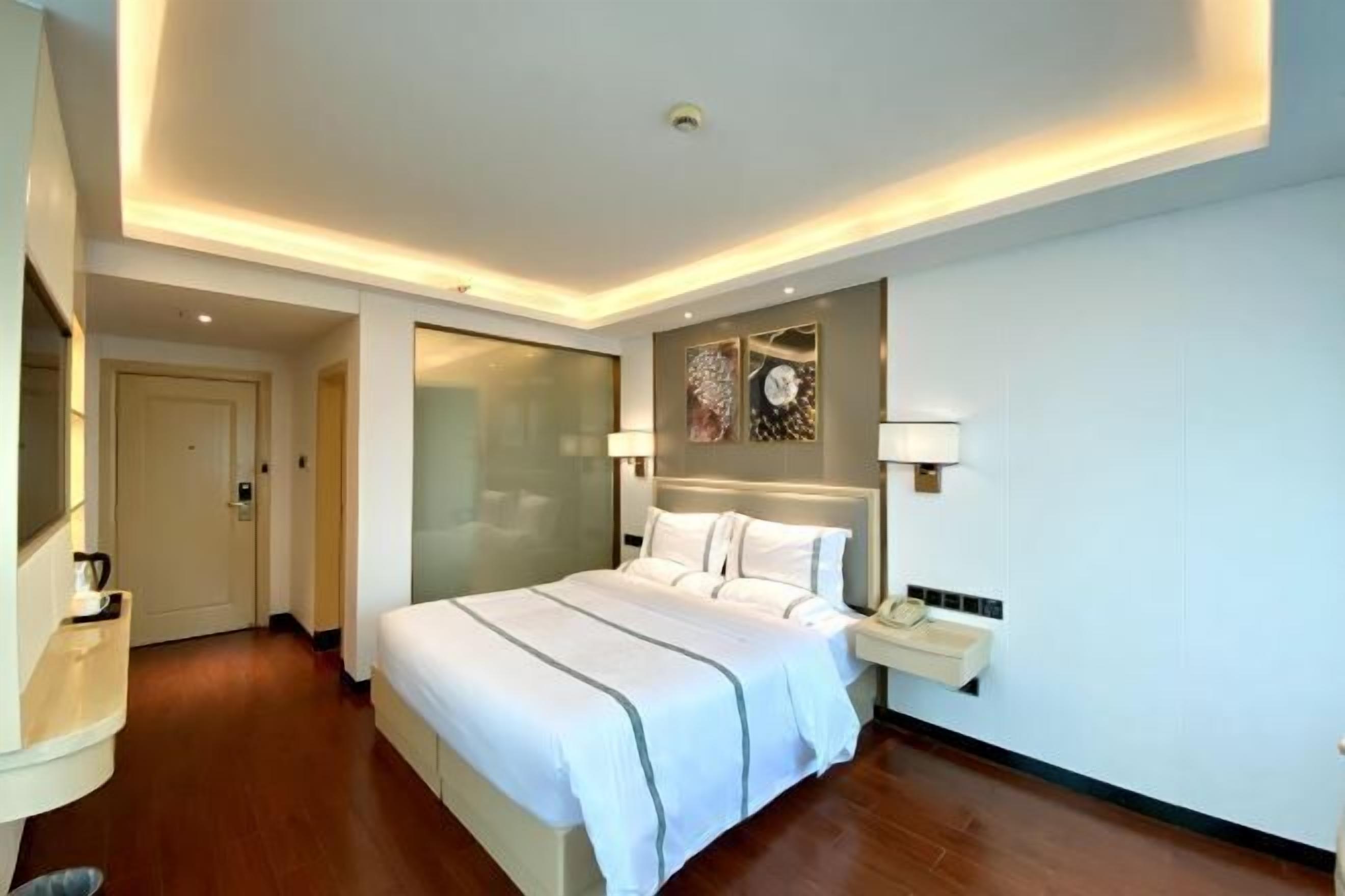 A modern hotel room with a large bed, bedside tables, a mirror, and a wall-mounted artwork.