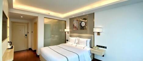 A modern hotel room with a large bed, bedside tables, a mirror, and a wall-mounted artwork.