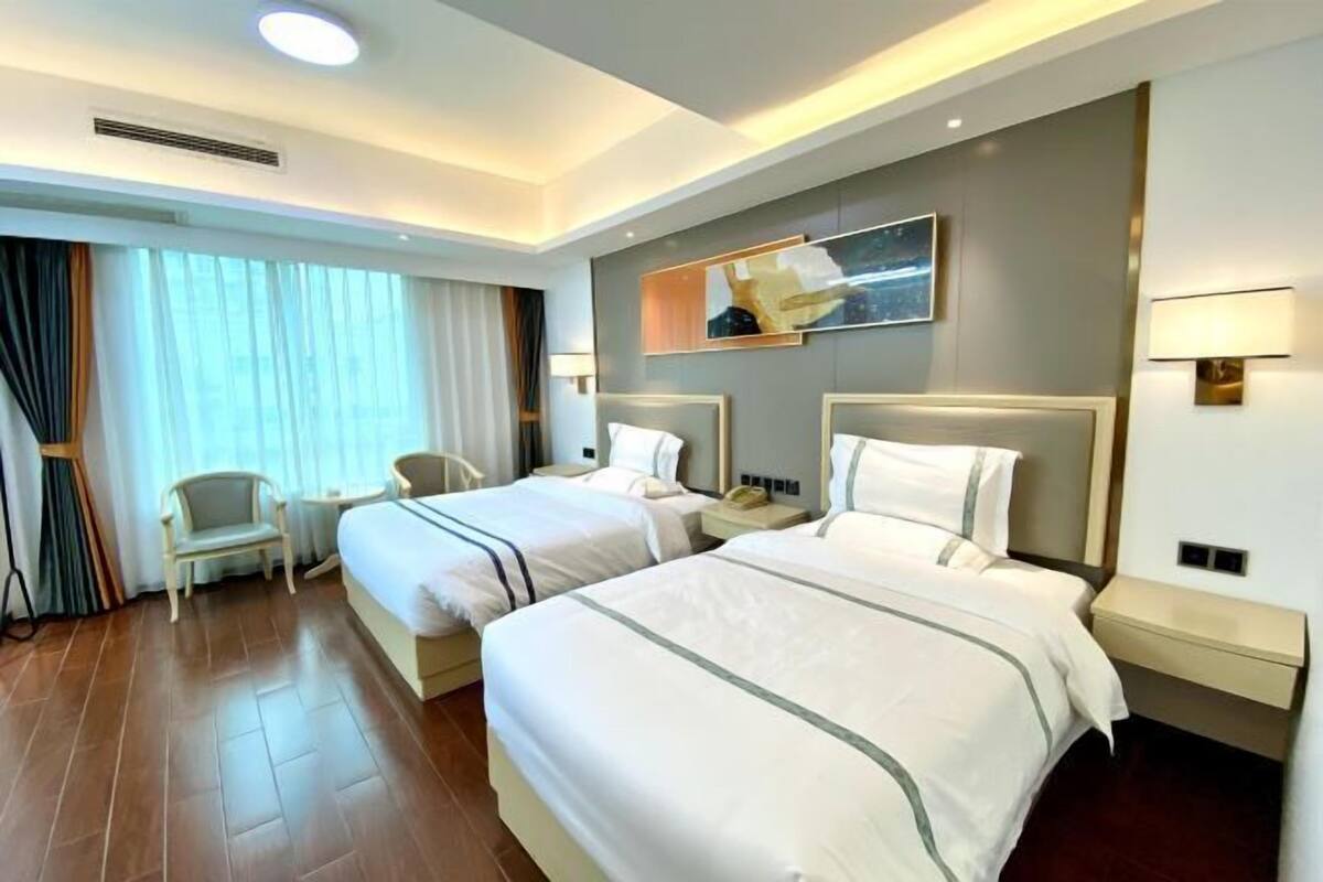 A hotel room with two beds, a desk, a chair, and a large window with curtains.