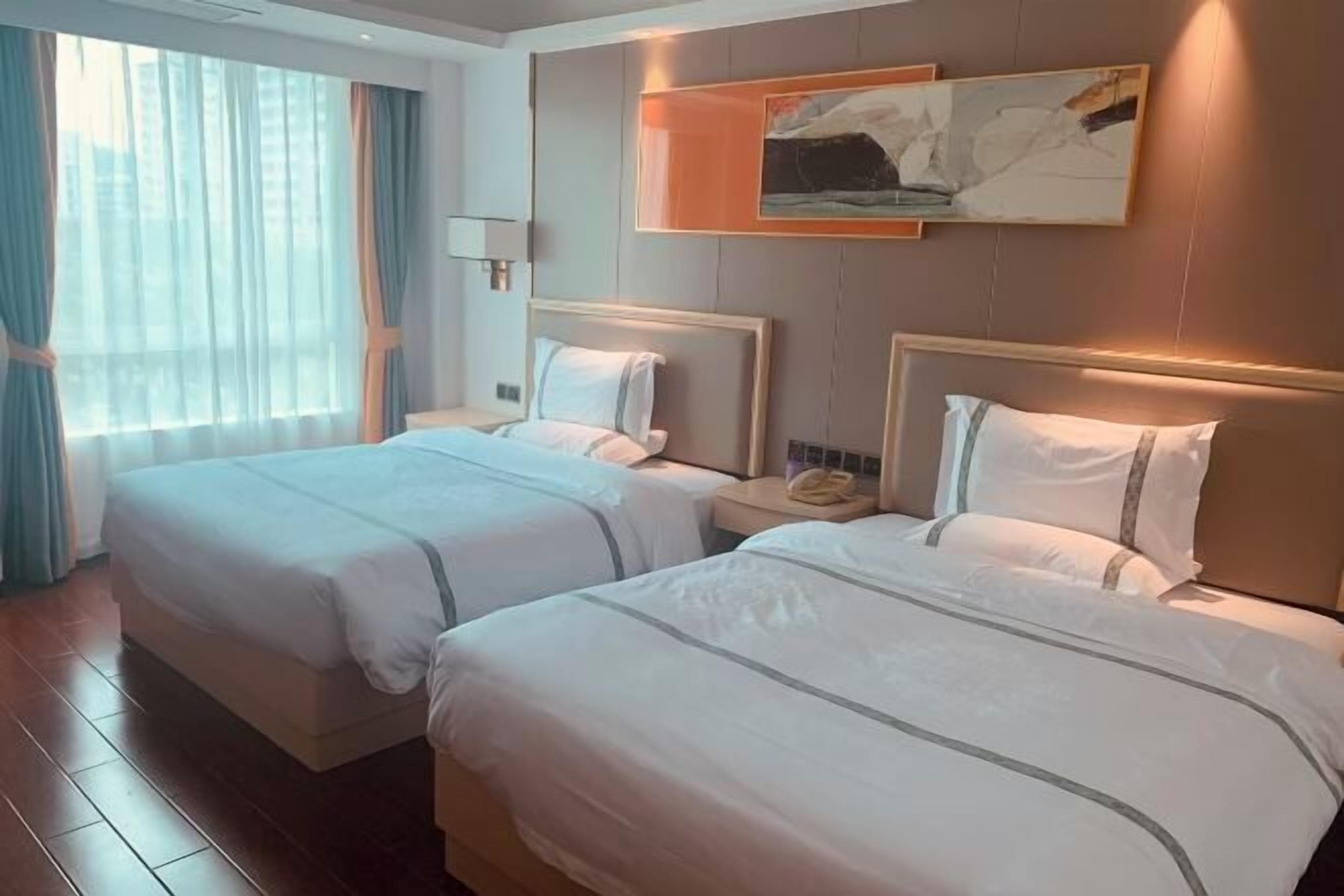 A hotel room with two beds, a large window with curtains, a painting on the wall, and a bedside lamp.