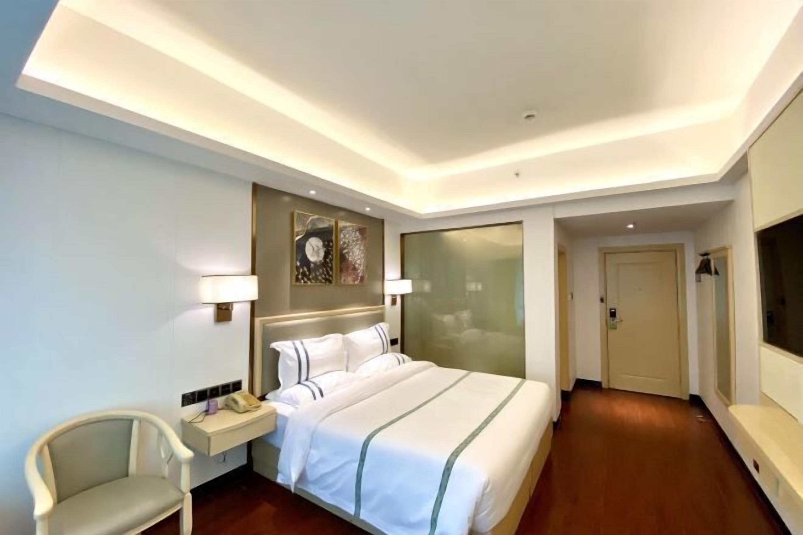 A hotel room with a bed, bedside table, lamp, chair, and a TV.