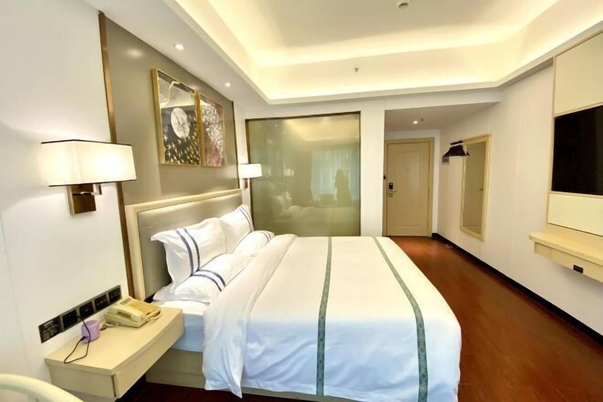 A hotel room with a bed, bedside table, lamp, and a TV.