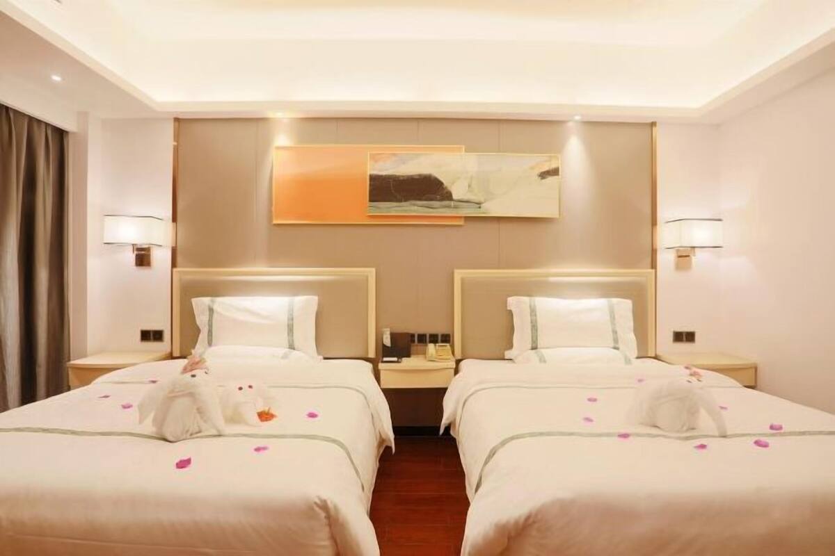 A hotel room with two beds, a large painting on the wall, and a nightstand between the beds.