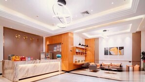 Un hall d’hôtel moderne avec un comptoir d’accueil en marbre, des éléments décoratifs en bois et un espace salon comprenant des canapés et une table basse.